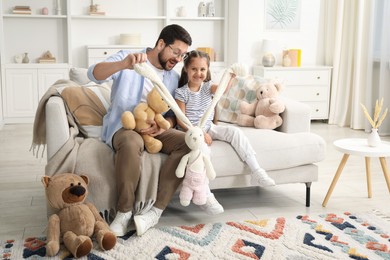 Photo of Father and his daughter playing with stuffed animals on sofa at home