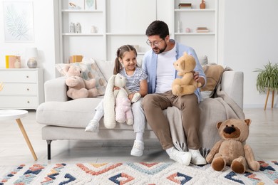 Photo of Father and his daughter playing with stuffed animals on sofa at home