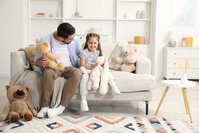 Photo of Father and his daughter playing with stuffed animals on sofa at home