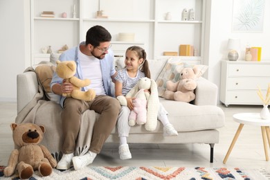 Photo of Father and his daughter playing with stuffed animals on sofa at home