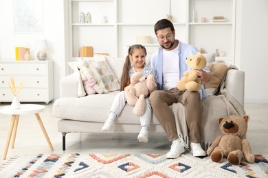 Photo of Father and his daughter playing with teddy bears on sofa at home