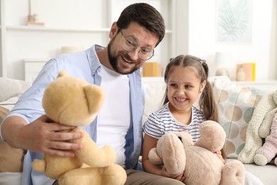 Photo of Father and his daughter playing with teddy bears on sofa at home