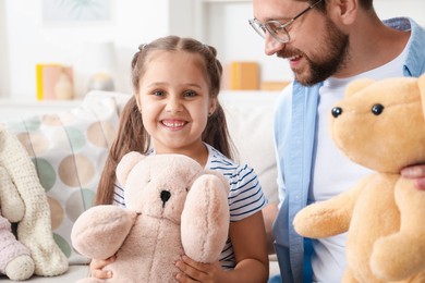Photo of Father and his daughter playing with teddy bears on sofa at home