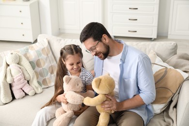 Photo of Father and his daughter playing with teddy bears on sofa at home