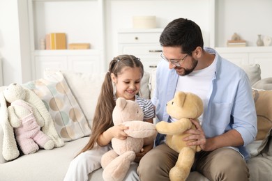 Photo of Father and his daughter playing with teddy bears on sofa at home