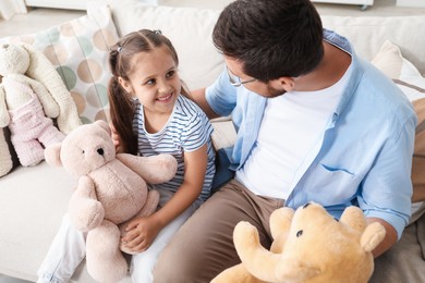 Photo of Father and his daughter playing with teddy bears on sofa at home