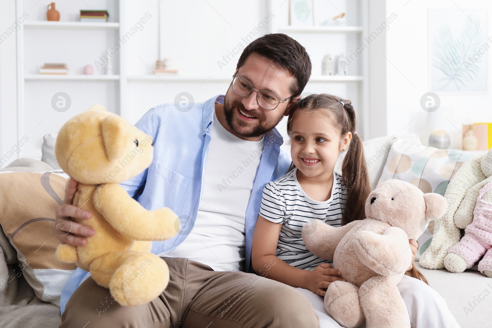 Father and his daughter playing with teddy bears on sofa at home Photo of Father and his daughter playing with teddy bears on sofa at home