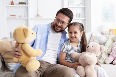 Photo of Father and his daughter playing with teddy bears on sofa at home