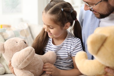Photo of Father and his daughter playing with teddy bears on sofa at home, closeup