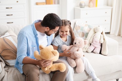 Photo of Father and his daughter playing with teddy bears on sofa at home