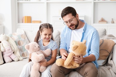 Photo of Father and his daughter playing with teddy bears on sofa at home