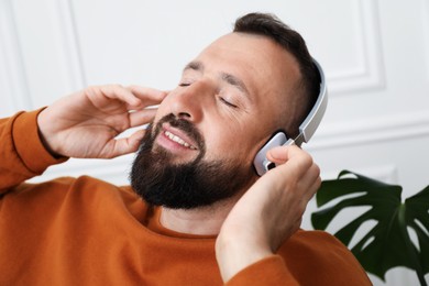 Photo of Harmony. Man listening to music in headphones at home, closeup