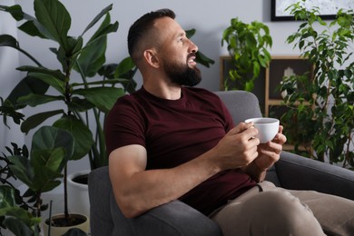 Photo of Harmony. Man with cup of drink in armchair at home