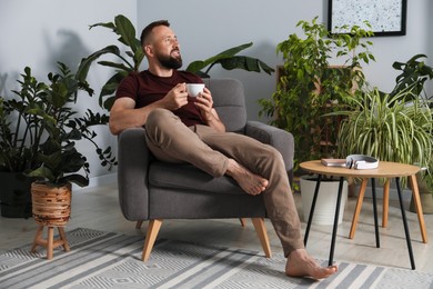 Photo of Harmony. Man with cup of drink in armchair at home
