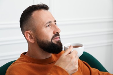 Photo of Harmony. Man with tea in armchair at home, closeup