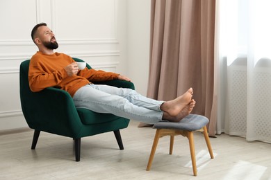 Photo of Harmony. Man with cup of drink in armchair at home