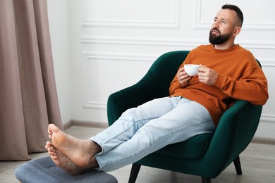 Photo of Harmony. Man with cup of drink in armchair at home