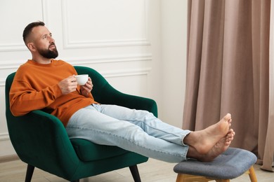 Photo of Harmony. Man with cup of drink in armchair at home