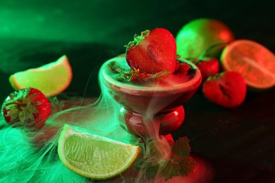 Photo of Hookah bowl with limes, strawberries, mint and smoke on black table, closeup