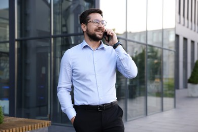 Photo of Happy businessman talking on phone near office building