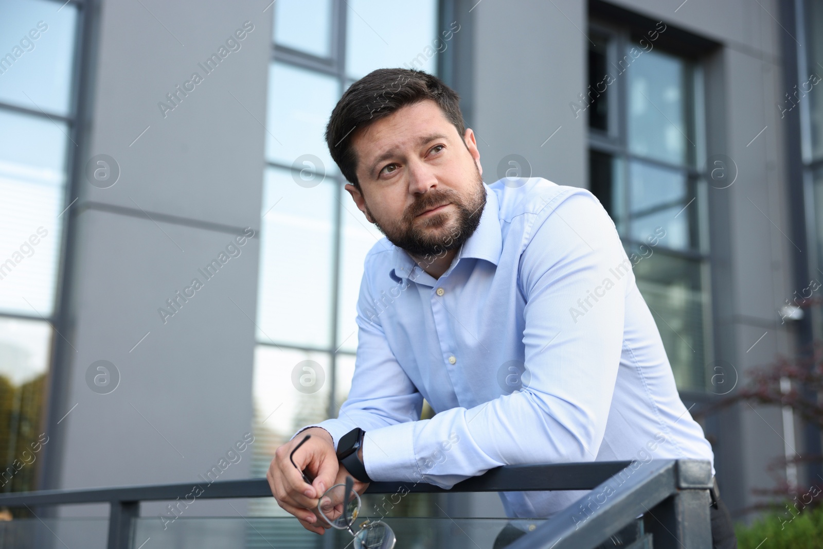 Tired businessman with glasses outside office building Photo of Tired businessman with glasses outside office building