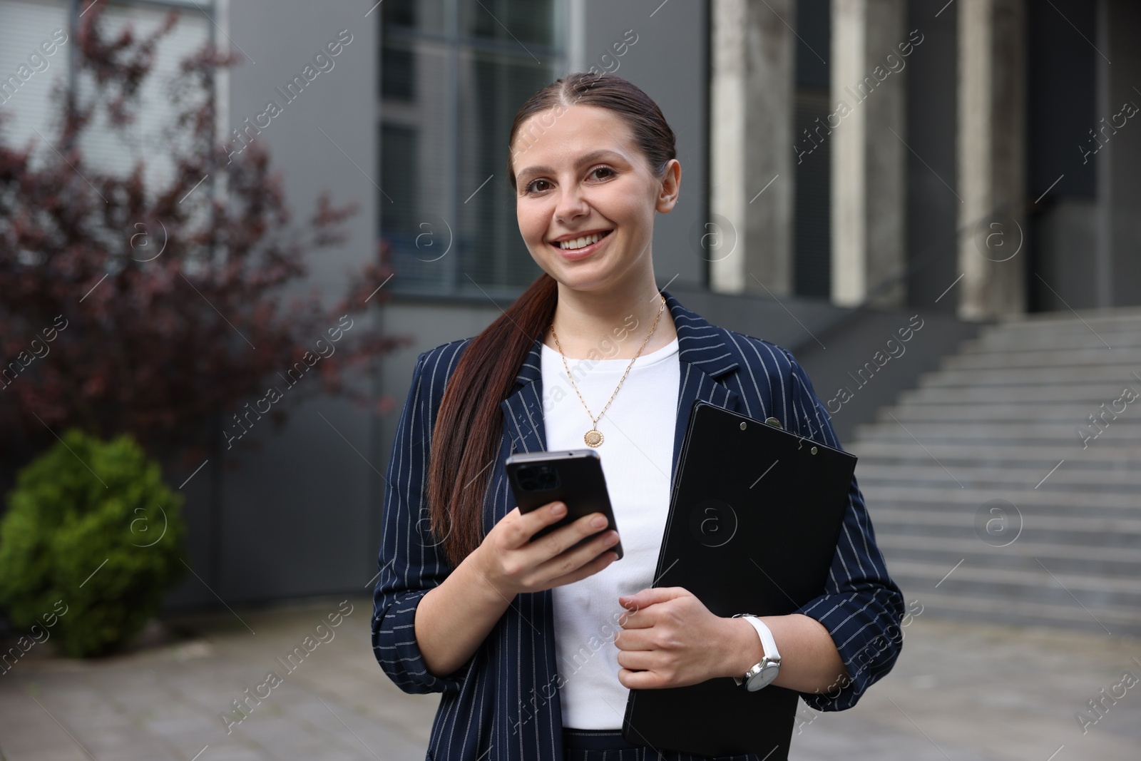 Happy businesswoman with smartphone near office building Photo of Happy businesswoman with smartphone near office building