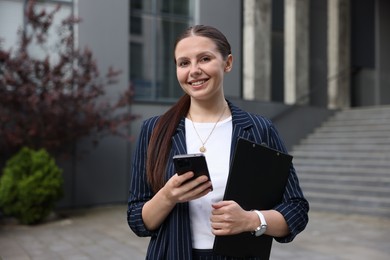 Photo of Happy businesswoman with smartphone near office building