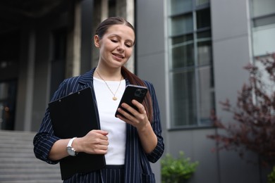 Photo of Happy businesswoman with smartphone near office building
