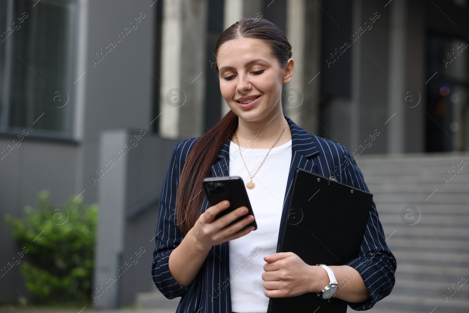 Photo of Happy businesswoman with smartphone near office building