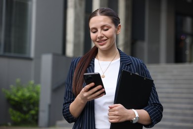Photo of Happy businesswoman with smartphone near office building