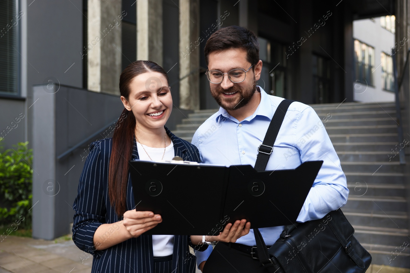 Happy coworkers with folder near office building Photo of Happy coworkers with folder near office building