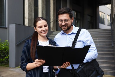 Photo of Happy coworkers with folder near office building