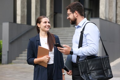 Photo of Happy coworkers with tablet and smartphone near office building