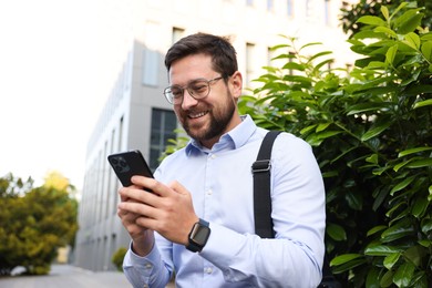 Photo of Successful businessman with smartphone near office building