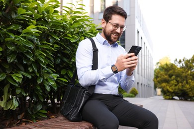 Photo of Successful businessman with smartphone on bench near office building