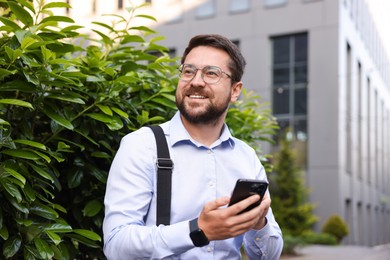 Photo of Successful businessman with smartphone near office building