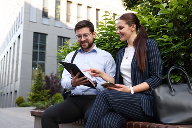 Photo of Happy coworkers discussing something on bench near office building