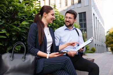 Photo of Happy coworkers discussing something on bench near office building