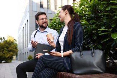 Photo of Happy coworkers discussing something on bench near office building