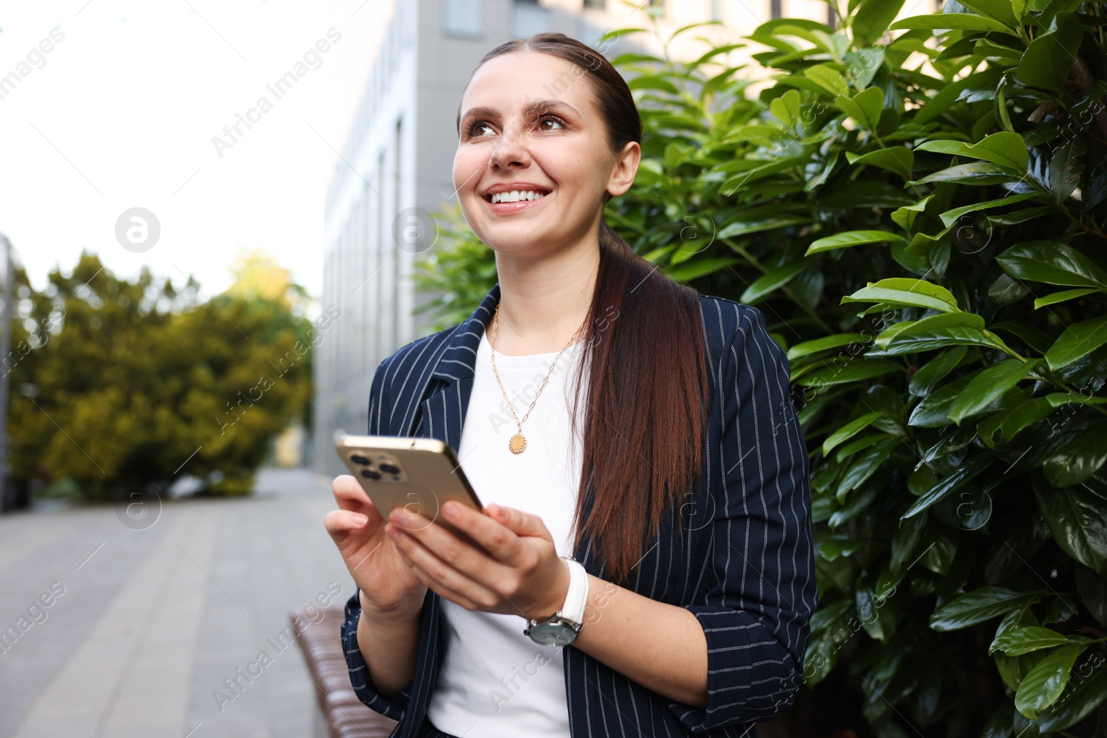 Photo of Successful businesswoman with smartphone near office building