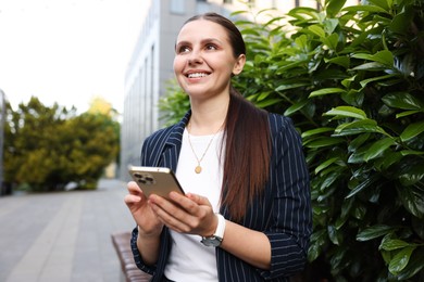 Photo of Successful businesswoman with smartphone near office building