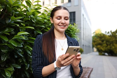 Photo of Successful businesswoman with smartphone near office building