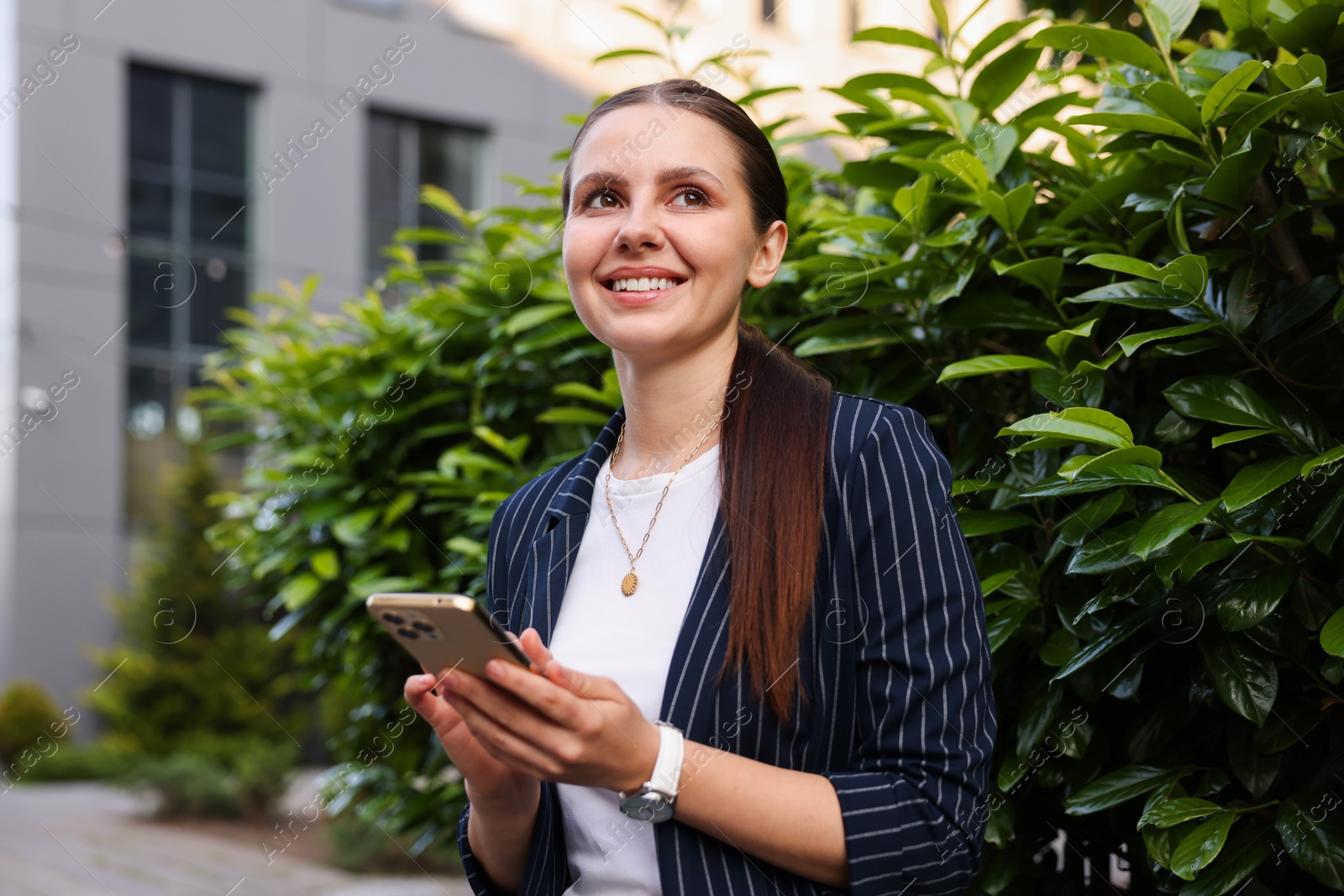 Photo of Successful businesswoman with smartphone near office building