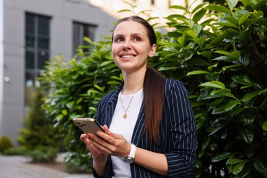 Photo of Successful businesswoman with smartphone near office building