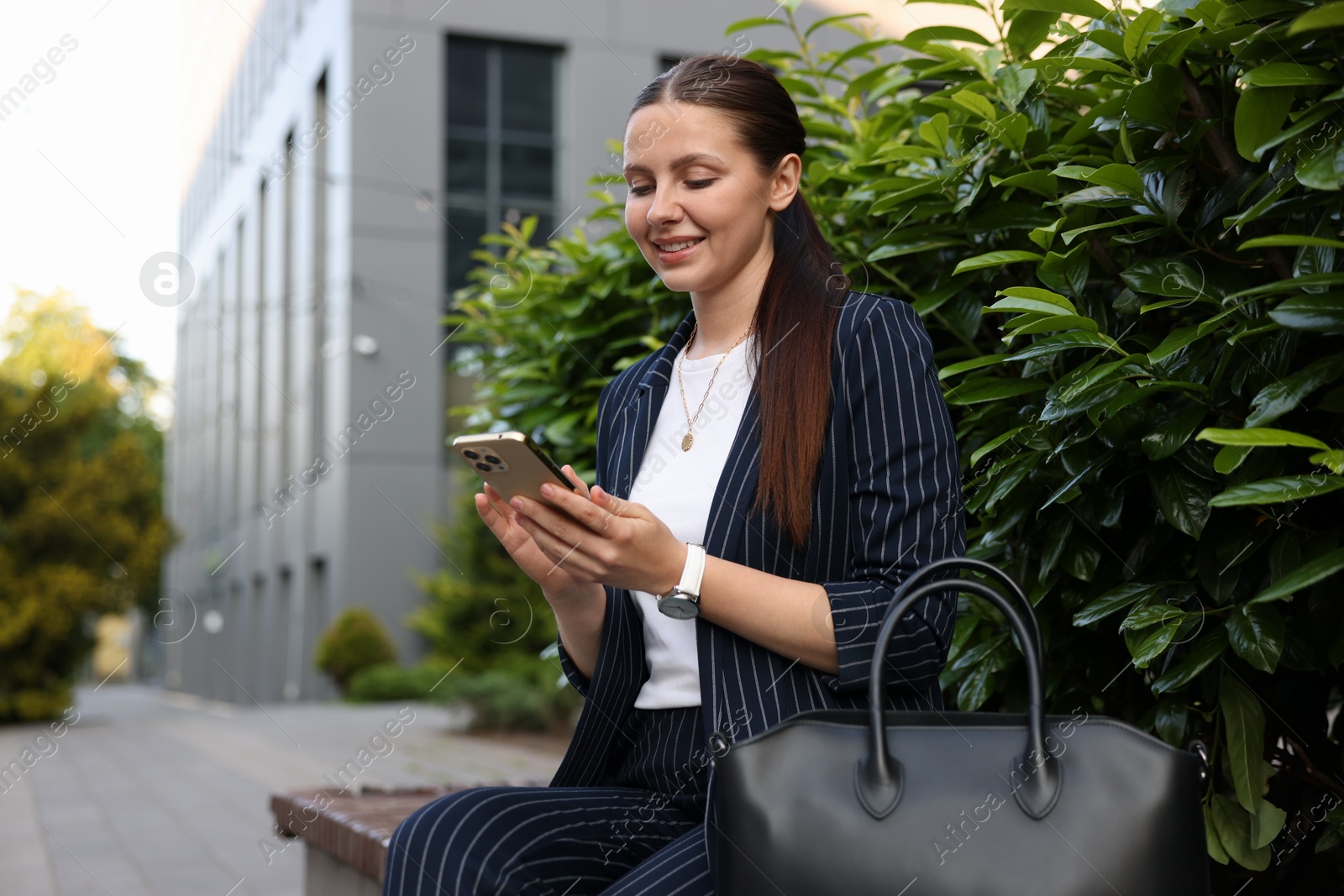 Photo of Successful businesswoman with smartphone near office building