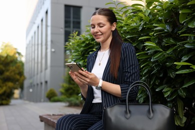 Photo of Successful businesswoman with smartphone near office building