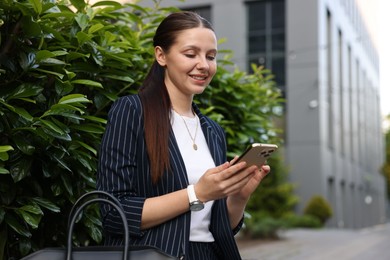 Photo of Successful businesswoman with smartphone near office building