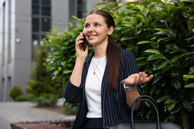 Photo of Successful businesswoman talking on phone near office building