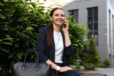 Photo of Successful businesswoman talking on phone near office building