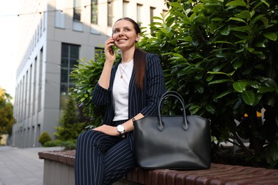 Photo of Successful businesswoman talking on phone near office building